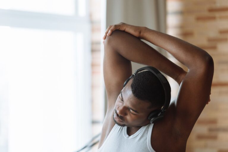Como escolher a melhor música para treinar em cada treino Homem de regata branca faz alongamento enquanto ouve música em fones de ouvido durante o treino